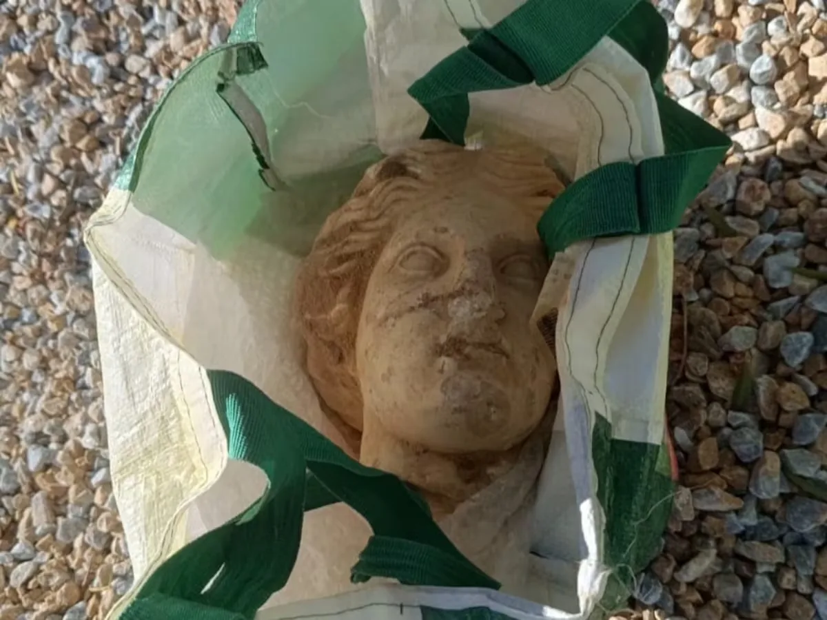 The amazing Venus of Alicante: a 2,000-year-old head peeks out among stones, large beer bottles, and a supermarket bag